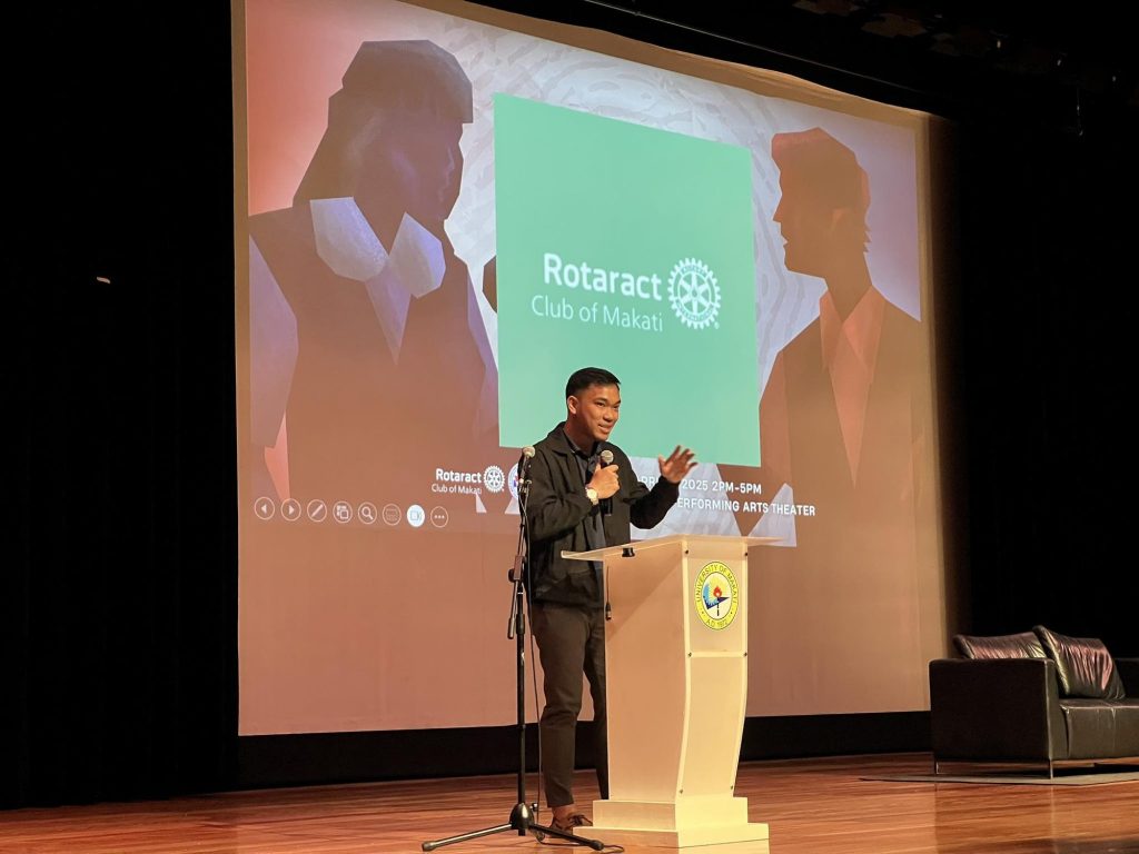 A Rotaract Club of Makati officer addresses the seminar from the stage podium, a club slide projected behind him.
