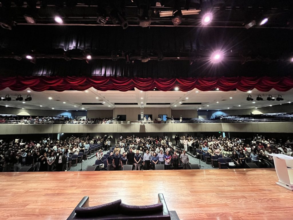A packed UMak Performing Arts Theater of over 900 first-time voters, seen from the stage.