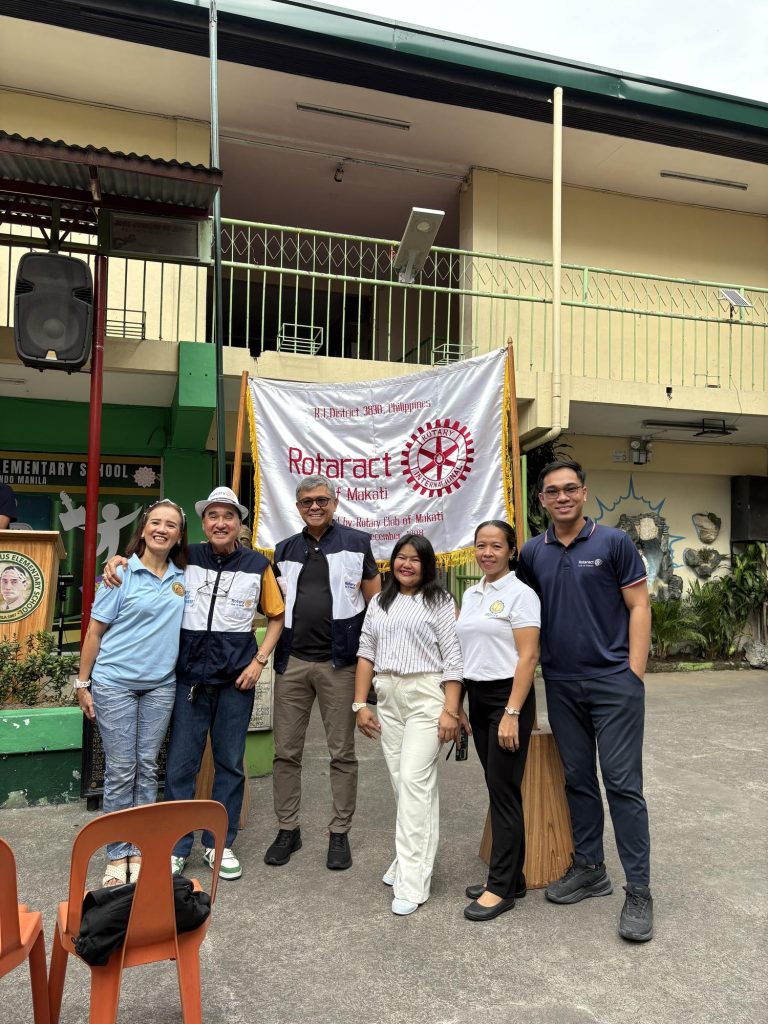 Volunteers and organizers pose with a Rotaract banner outside Jose Corazon de Jesus Elementary School.