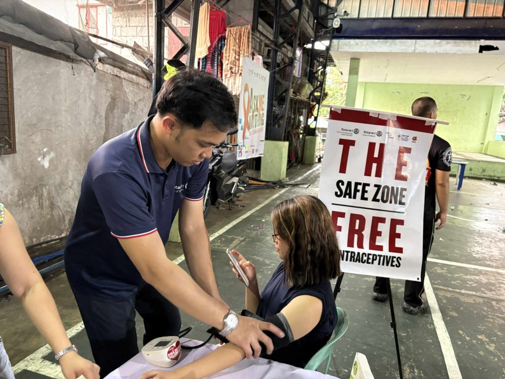 A Rotaractor checks a participant’s blood pressure beside the “Safe Zone: free contraceptives” banner.